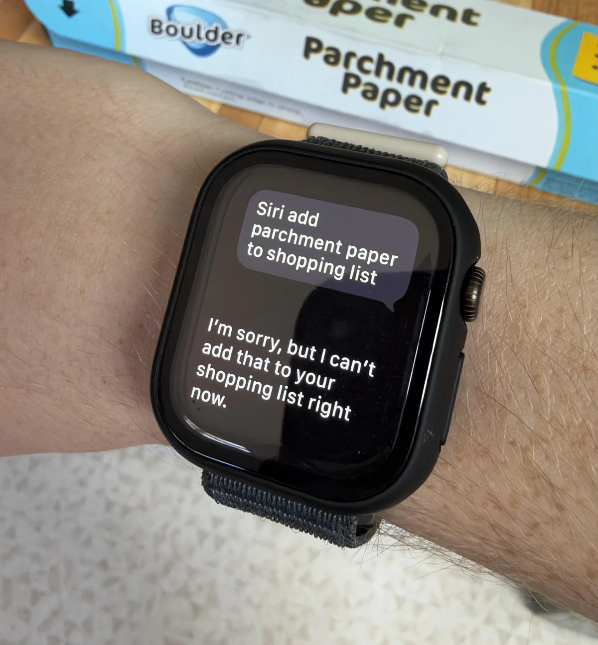 An Apple Watch shows a correctly transcribed parchment-paper shopping-list request followed by Siri’s refusal to add it.